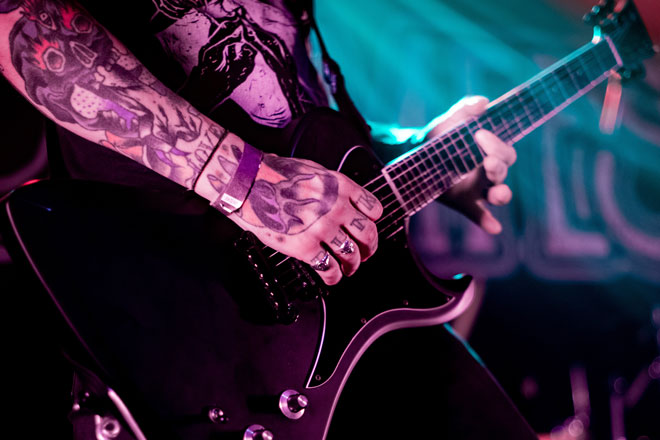 Close up of the heavily tattooed hand, forearm and guitar of Guitarist vocalist from Acid Throne performing in London