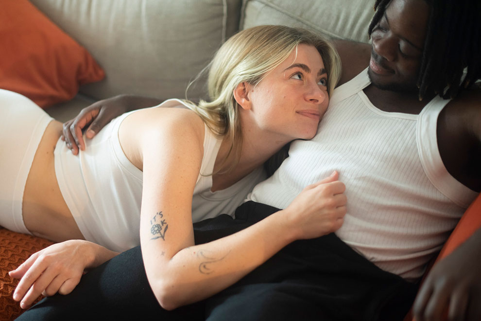 Young couple lying together on a sofa, natural light couples portrait in urban flat

