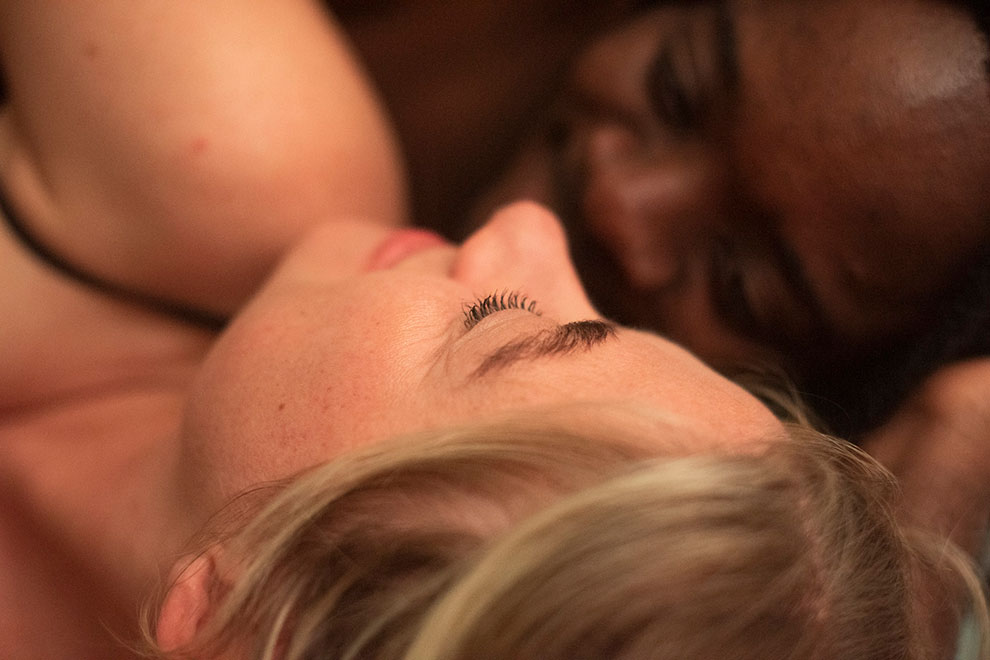 Close-up of couple lying together in bed, tender moment with soft indoor lighting
