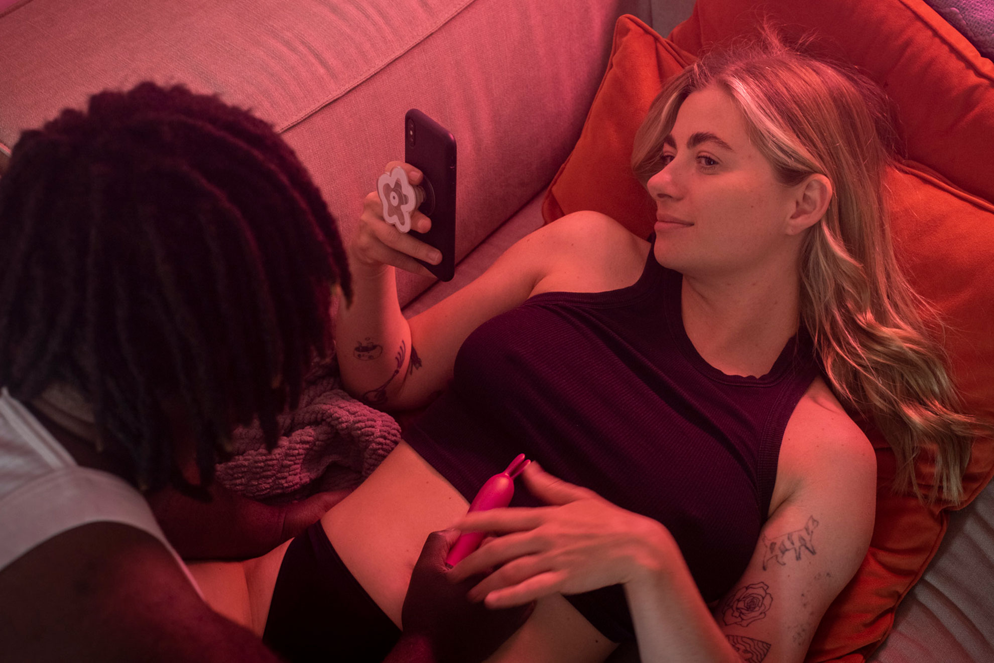 Young couple sitting close in red-lit room, sharing music and affection, stylised home shoot