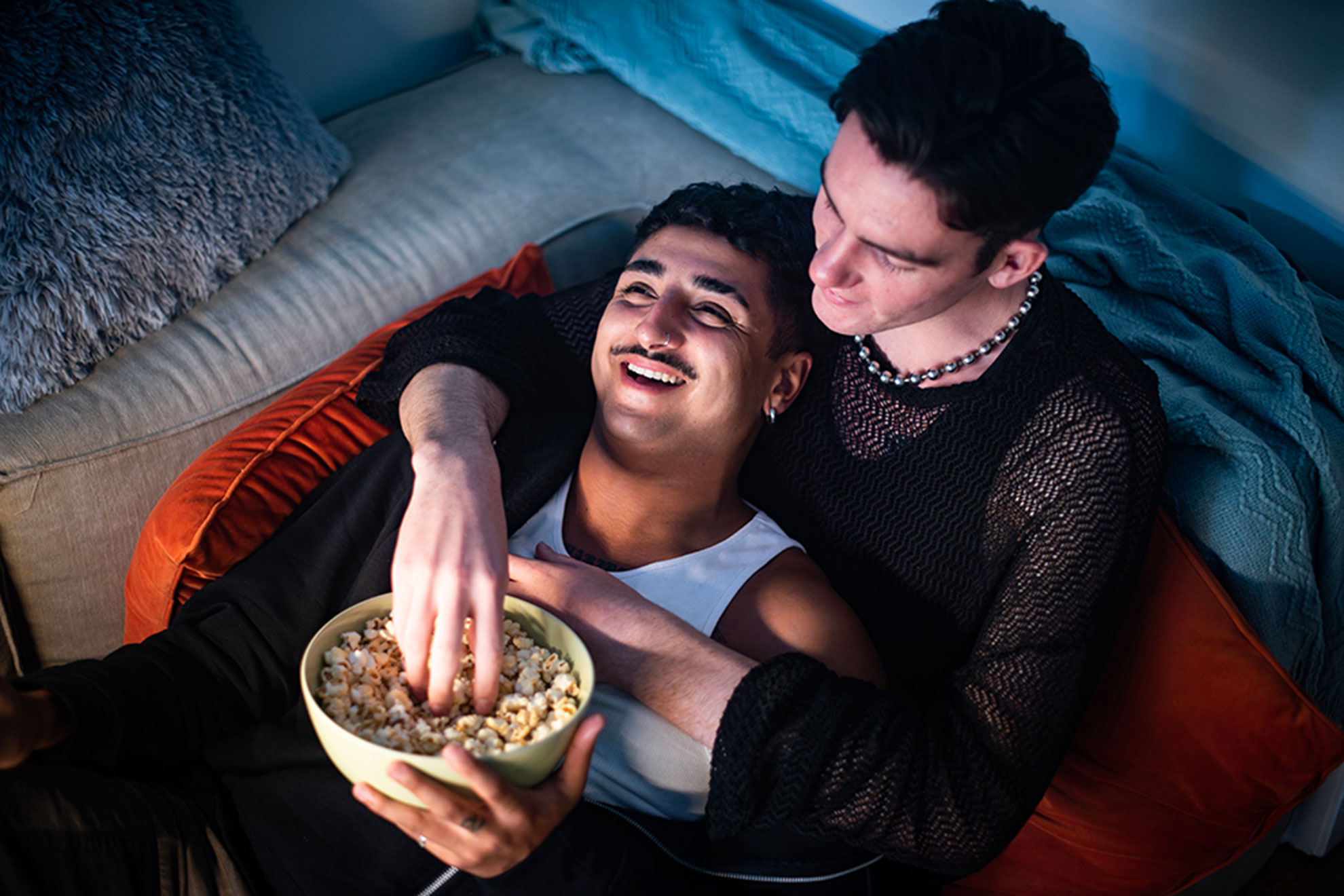 Male couple watching sharing popcorn watching a film together while cuddling