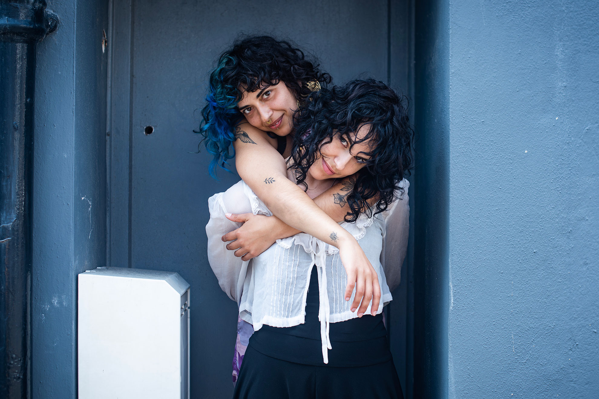 Two women embracing affectionately in a doorway, LGBTQ+ couples portrait with warm tones
