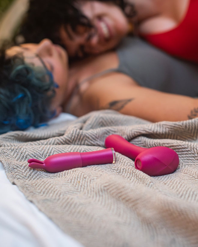 Close-up of massagers on a bed with a female couple lying beside them