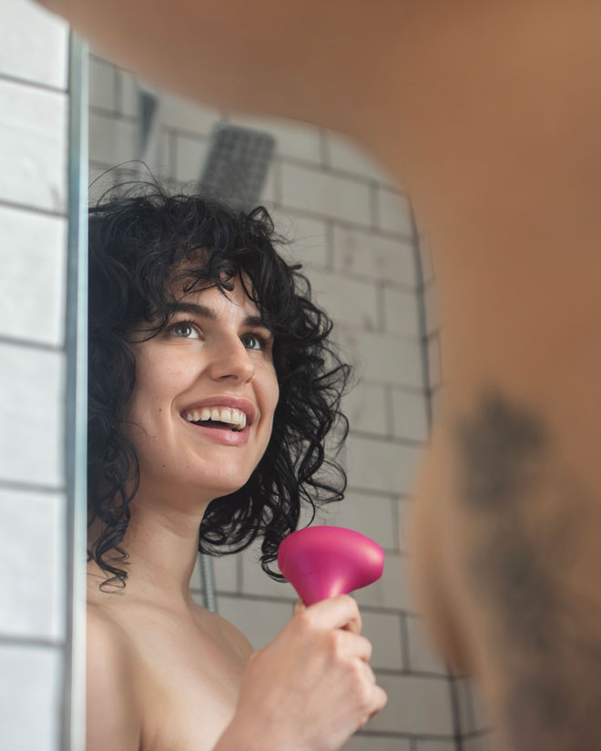 Smiling woman in a shower holding a pink massager massager