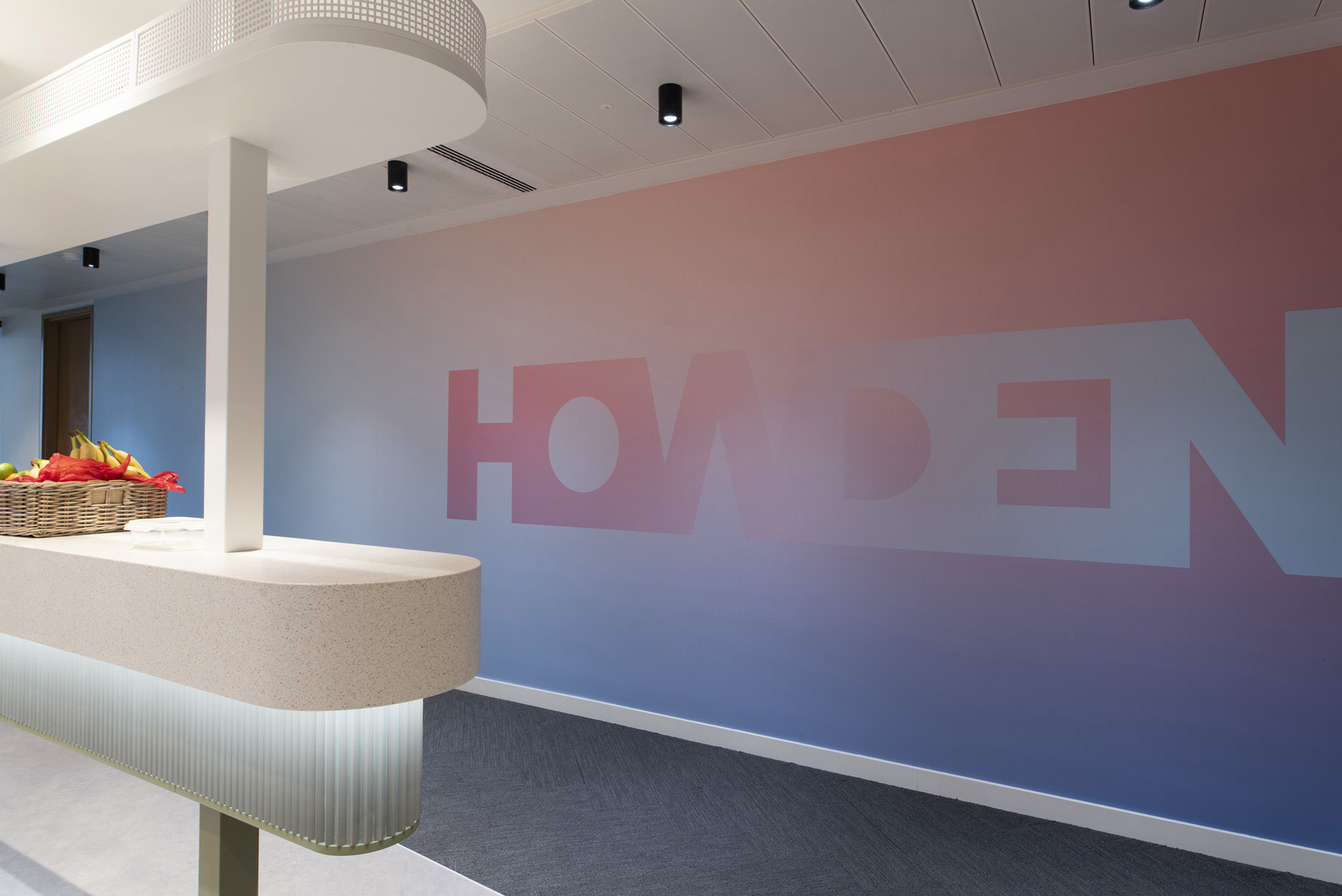 Modern reception counter with basket of fruit on the left and a gradient wall.