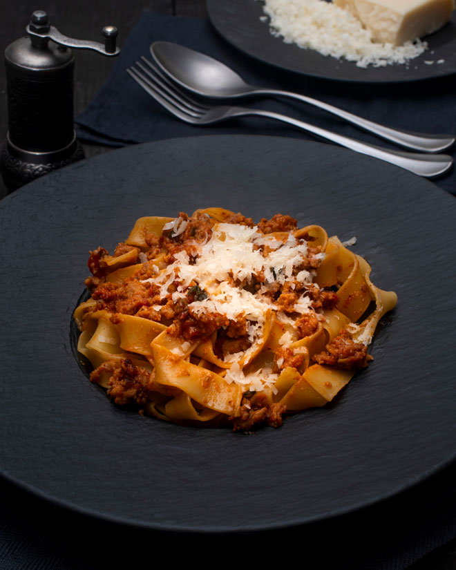 Close-up of pasta with rich tomato sauce and melted cheese, presented on a black plate