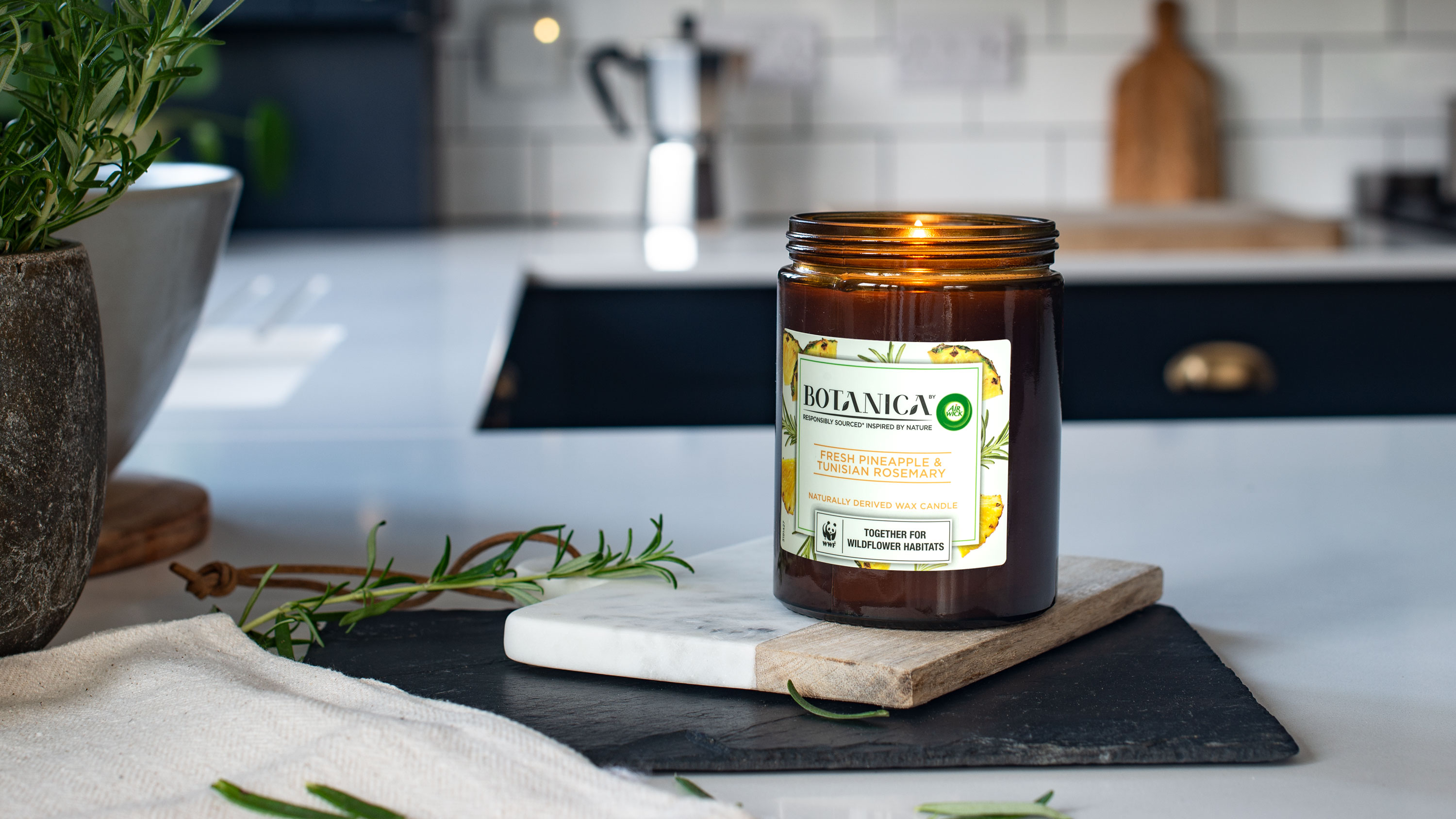 Botanica scented candle with fresh pineapple and rosemary on a kitchen counter