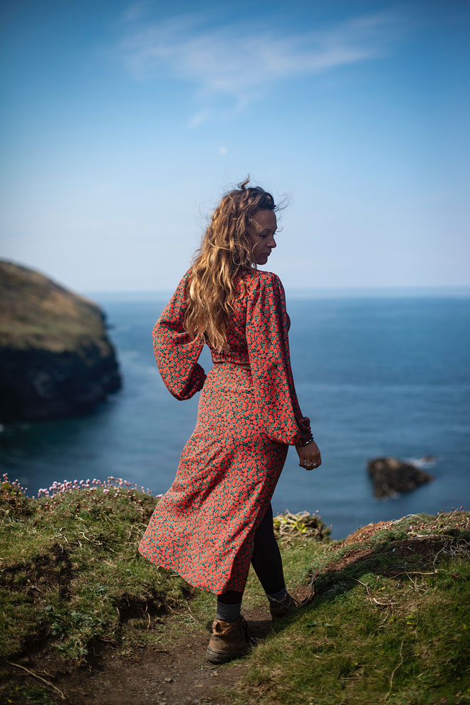 Woman in red dress gazing out over the water, windswept fashion shoot by the ocean

