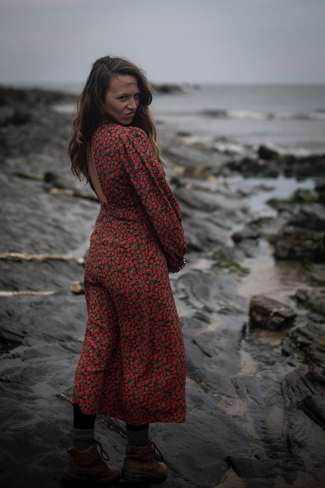 Woman in red dress walking on a rocky shoreline, UK outdoor fashion shoot
