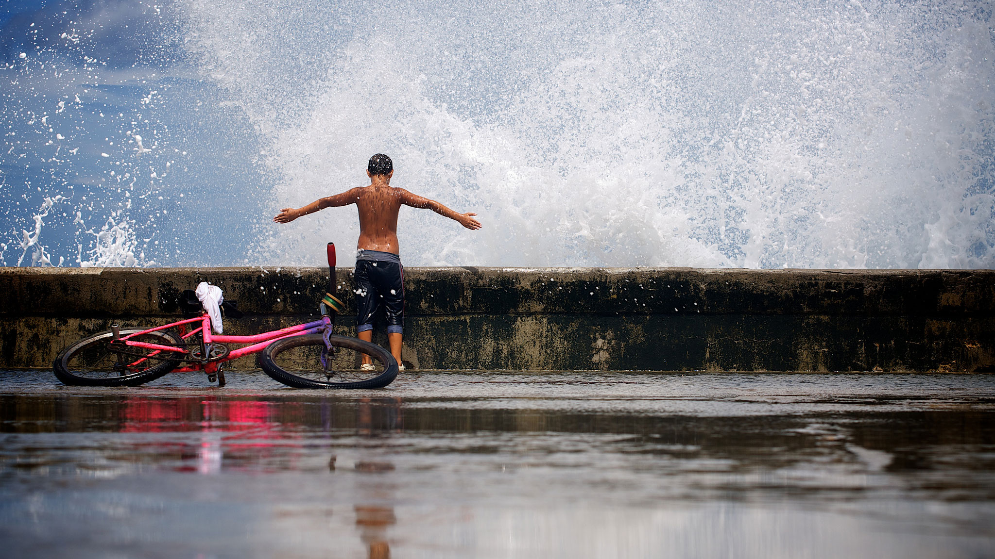 A young boy on the sea front in Havana lettimself be splashed by a huge wave