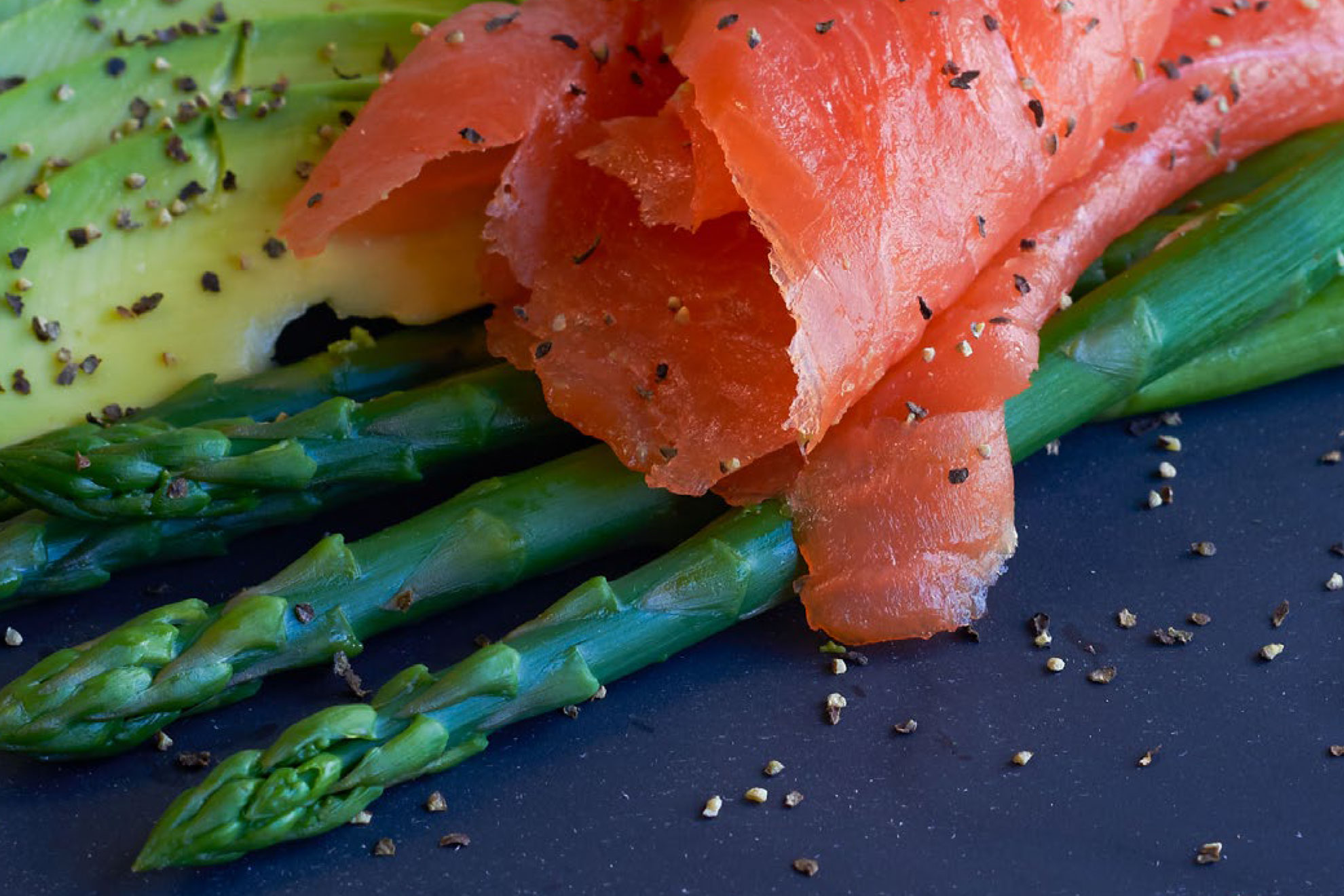 Smoked salmon slices and avocado on steamed asparagus, seasoned with cracked black pepper