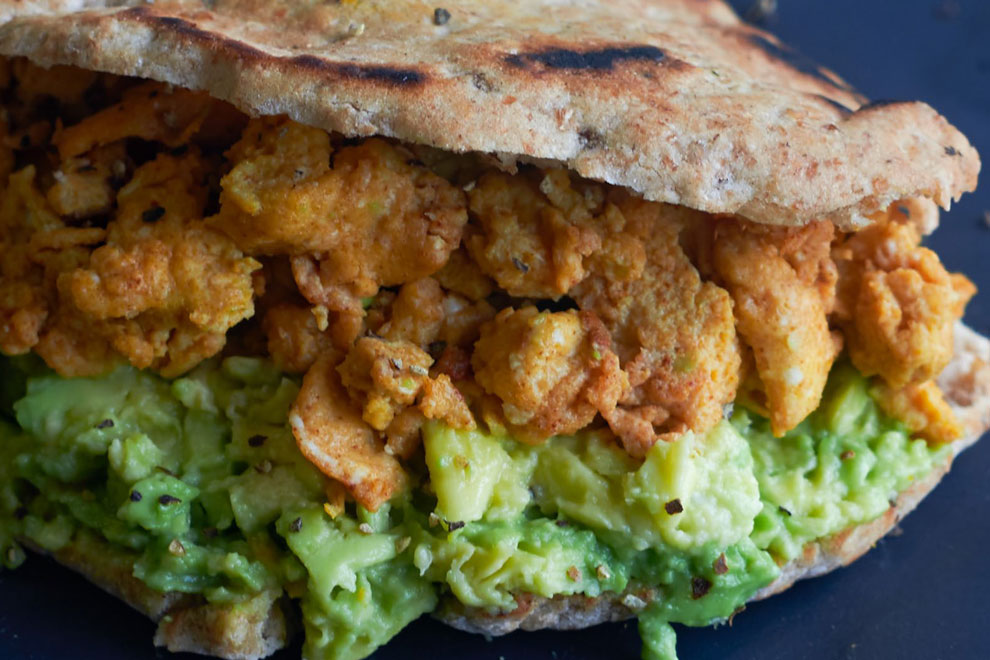 Flatbread sandwich filled with crushed avocado and crispy chicken pieces, for street food styling