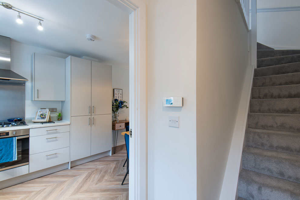 View from a hallway into a modern, sleek kitchen with fitted appliances and units