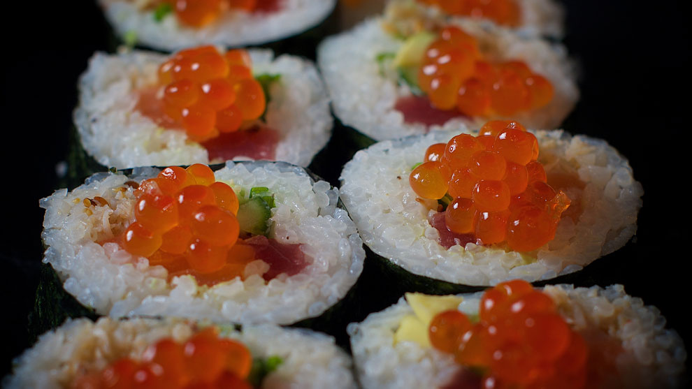 Fresh salmon roe sushi rolls with rice and sesame seeds, on a dark serving plate